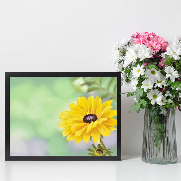 Yellow daisy flower stretched canvas print withing a black floating frame on shelf next to a vase of flowers