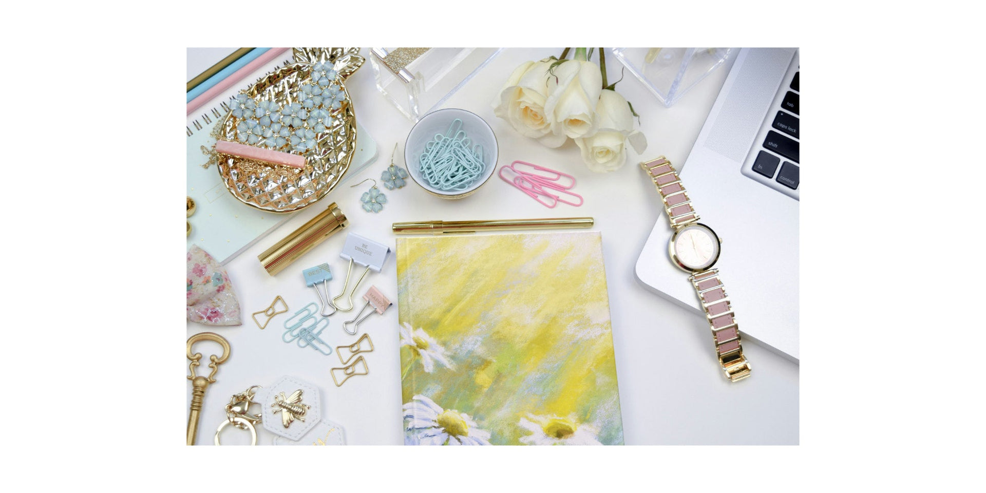 Yellow journal with white daisy flower design on a desk with stationery, laptop and ladies watch