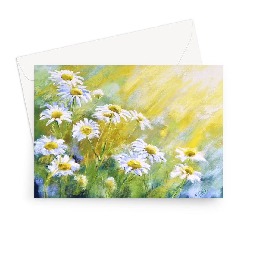 Landscape format greeting card featuring a painted meadow of white daisies with yellow centers and a soft yellow-green background, shown with a white envelope behind it on a light gray studio background.