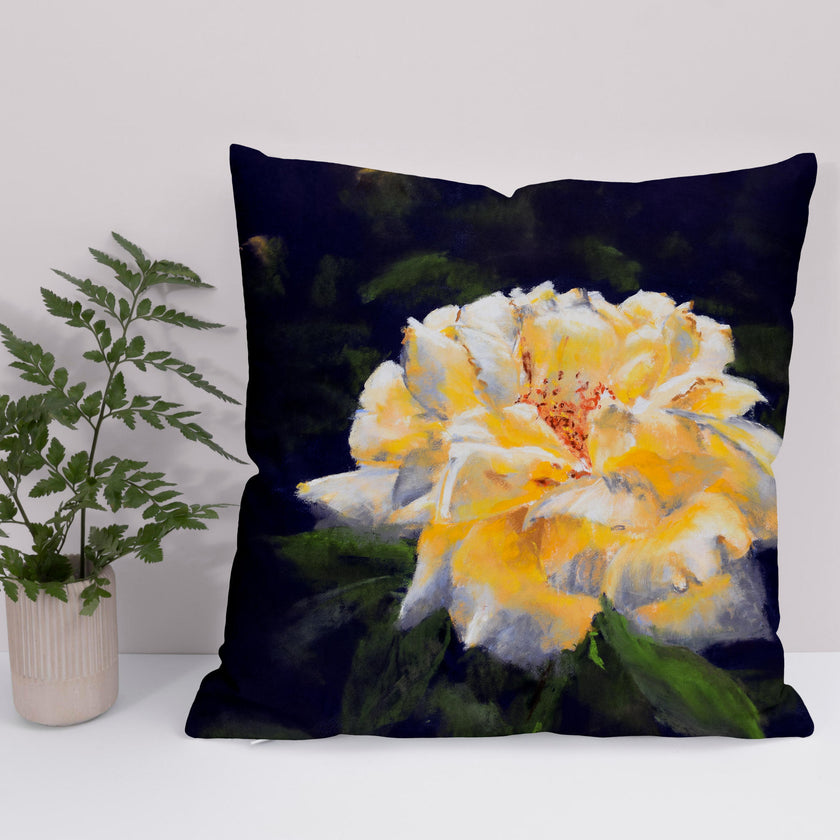 A square throw cushion with a golden yellow rose on a dark violet background, displayed in a home setting.