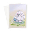 Greeting card with a white bunny holding a blue watering can among the daisy flowers