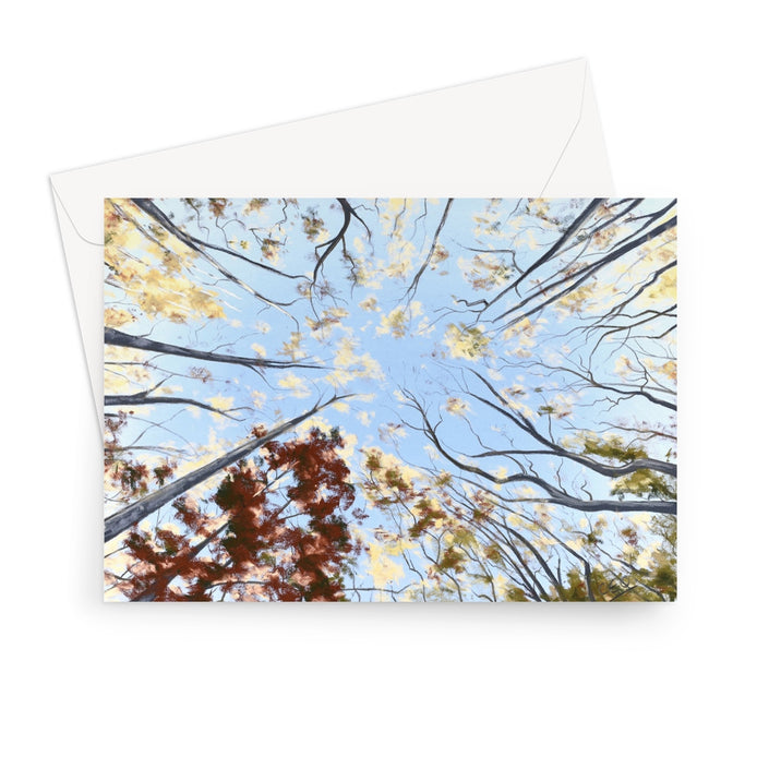 A landscape format greeting card featuring an upward-looking view of tree branches reaching toward a blue sky, with yellow and brown autumn leaves, shown with a white envelope behind it on a white background.