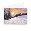 A landscape format greeting card featuring a snowy landscape with bare trees and a warm orange sky, shown with a white envelope behind it 