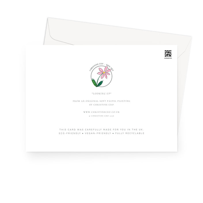 A white greeting card with a soft pink flower and green leaves, shown with a white envelope behind it on a light gray background.