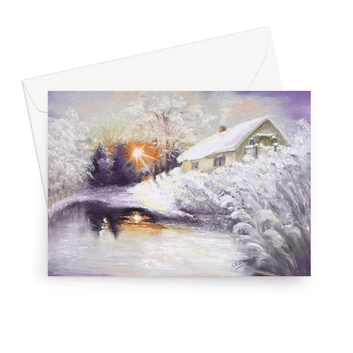 A landscape format greeting card featuring a winter landscape painting with a snow-covered house, trees, and a reflective stream, shown with a white envelope behind it 