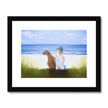 Boy and dog sitting overlooking the beach. Painting. Art print in black frame with white mount