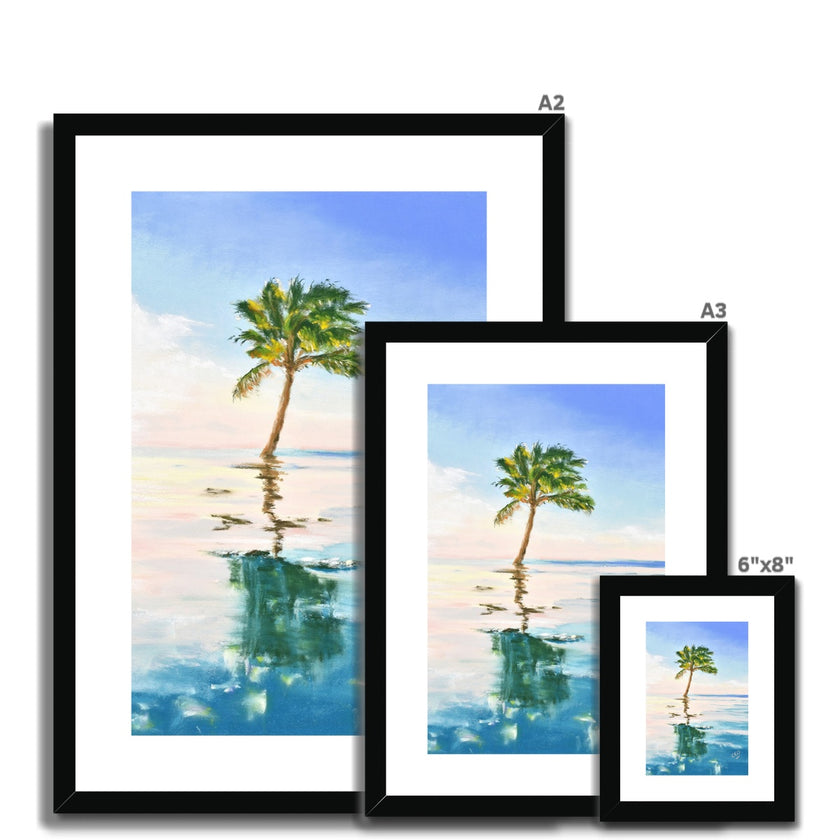 Palm tree set against blue sky and reflecting in clear turquoise water. Fine art print in a black frame with a white mount. Different sizes, smallest at the front.